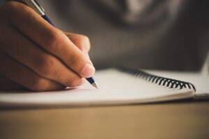 Hands writing in notebook on desk. 