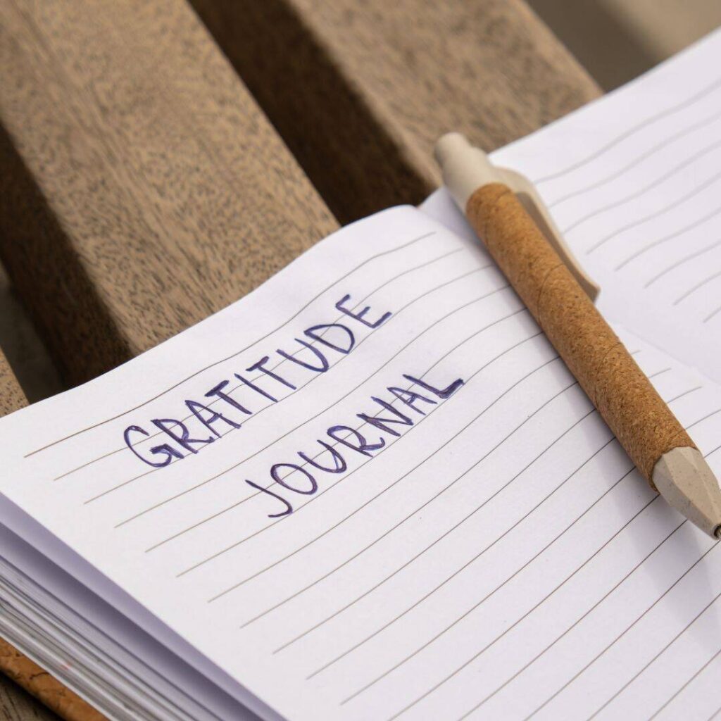 Gratitude journal written in black pen on notebook paper with brown colored pen laying on notebook.