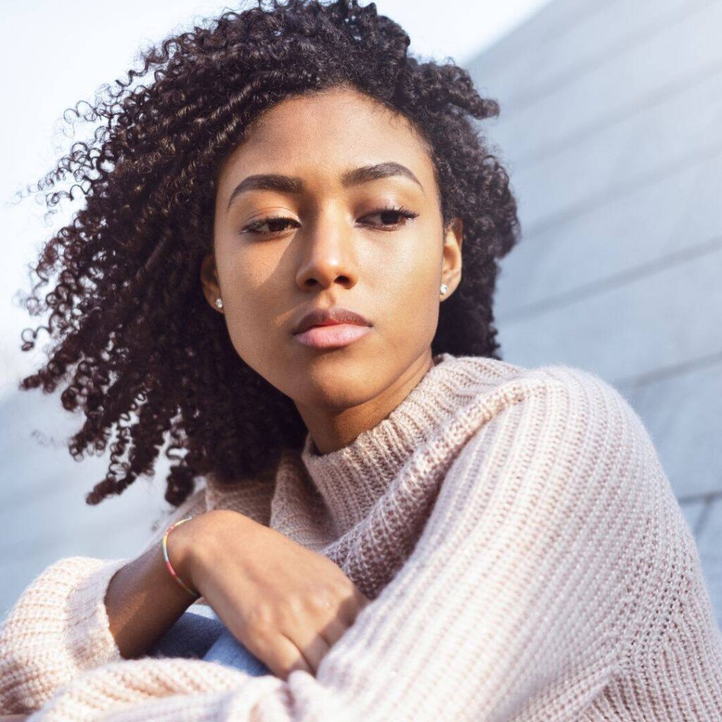 Black woman feeling sad and emotional looking down with her arms crossed.