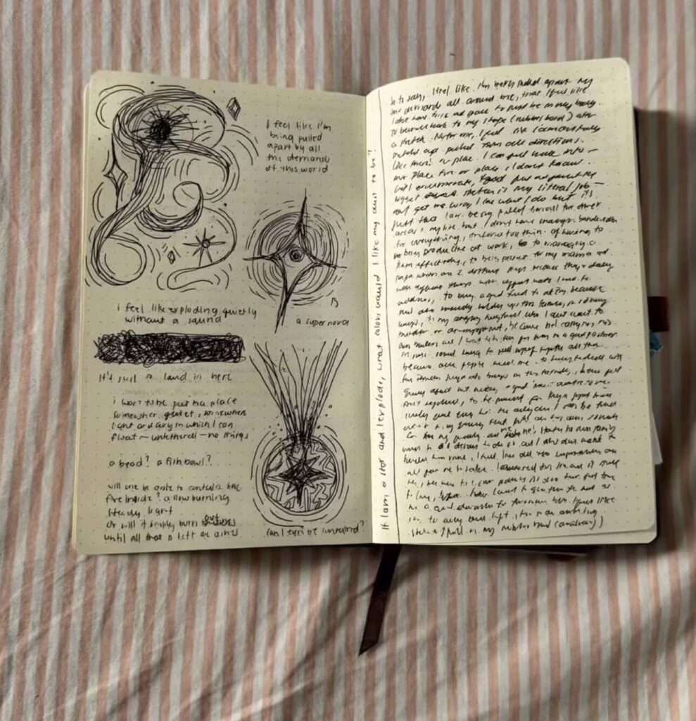 A journal is opened to two pages of star-like doodles and dense written text. The journal is laid flat against a background of pink and white striped cloth.
