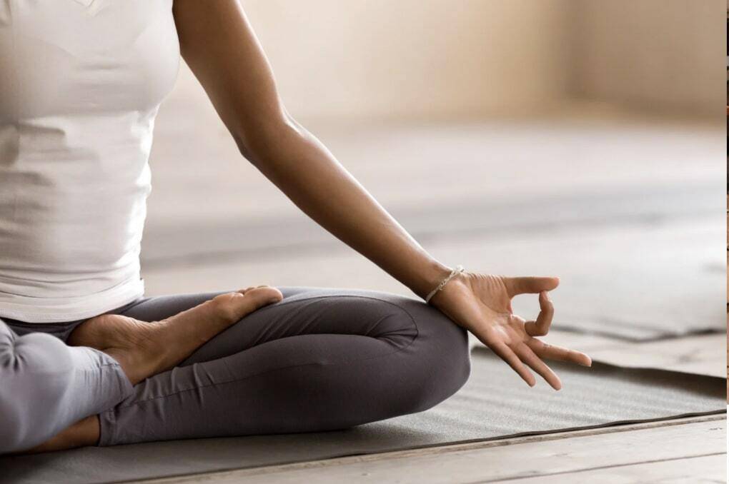 A black woman is sitting on a yoga mat in a meditation pose.