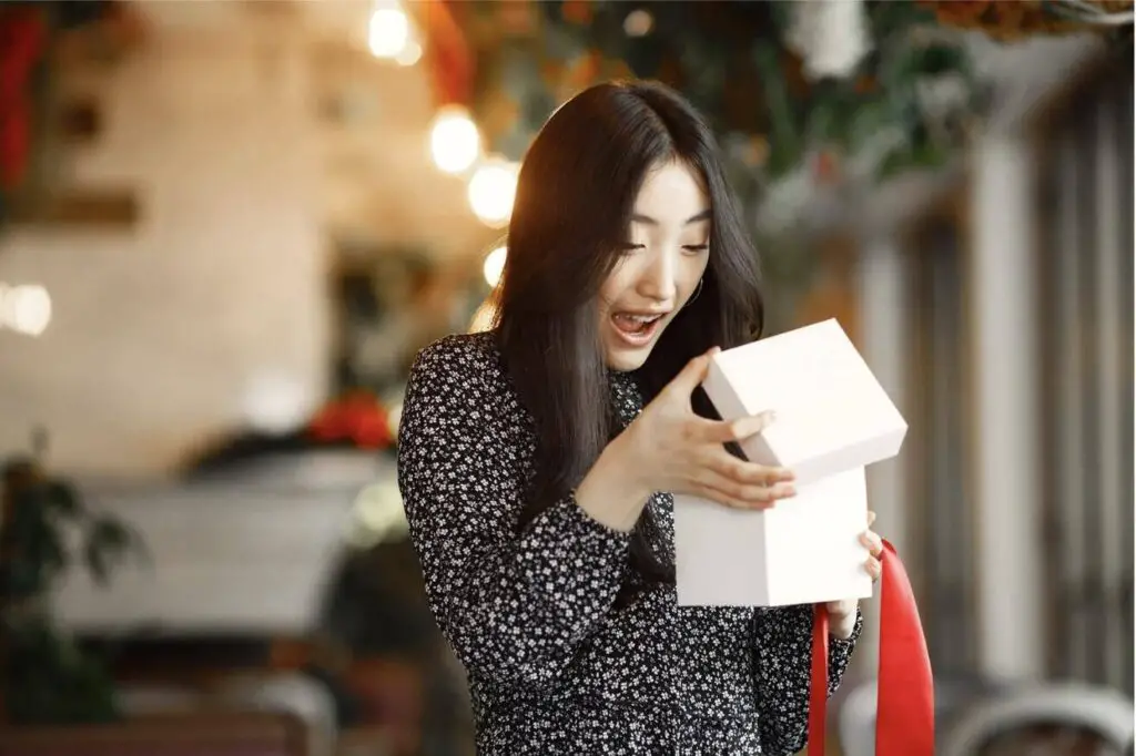 An Asian woman is looking into an open, white gift box with a surprised expression on
her face.