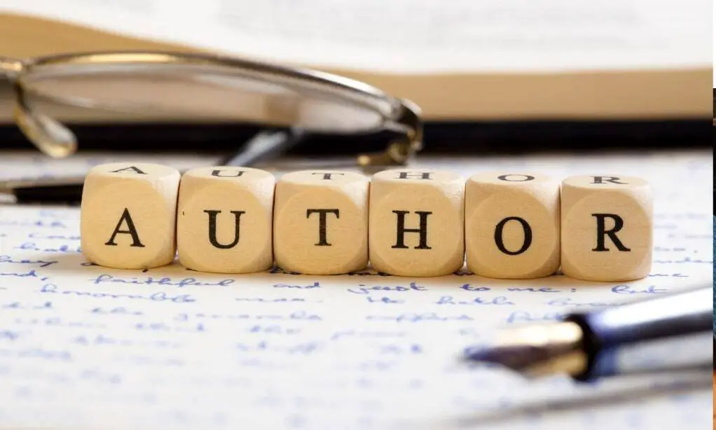  Six small wooden blocks, each with one letter on it, are lined up to spell
“AUTHOR.” They are sitting on a piece of paper that has writing in blue ink on it. Part of a quill
shows in the foreground, and part of a pair of glasses shows in the background.