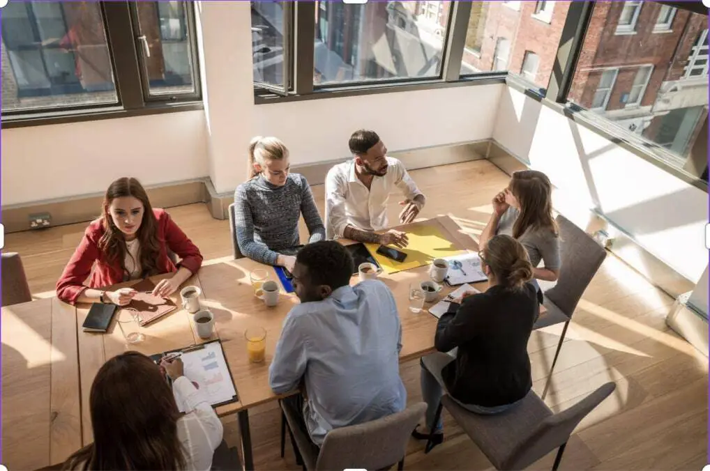 A group of men and women is sitting at a conference table in a room with sunlight
streaming through the windows. They have notebooks and coffee dispersed among them.