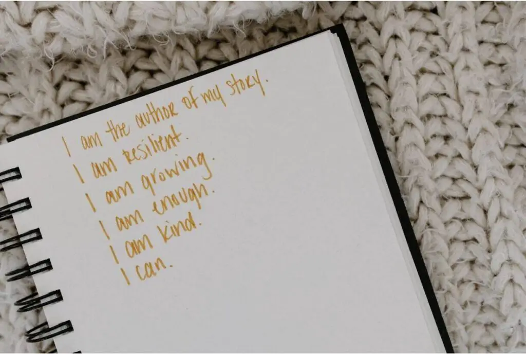 A journal is lying open on a carpet-like material. On the page in yellow marker ink, there are various positive affirmations written out