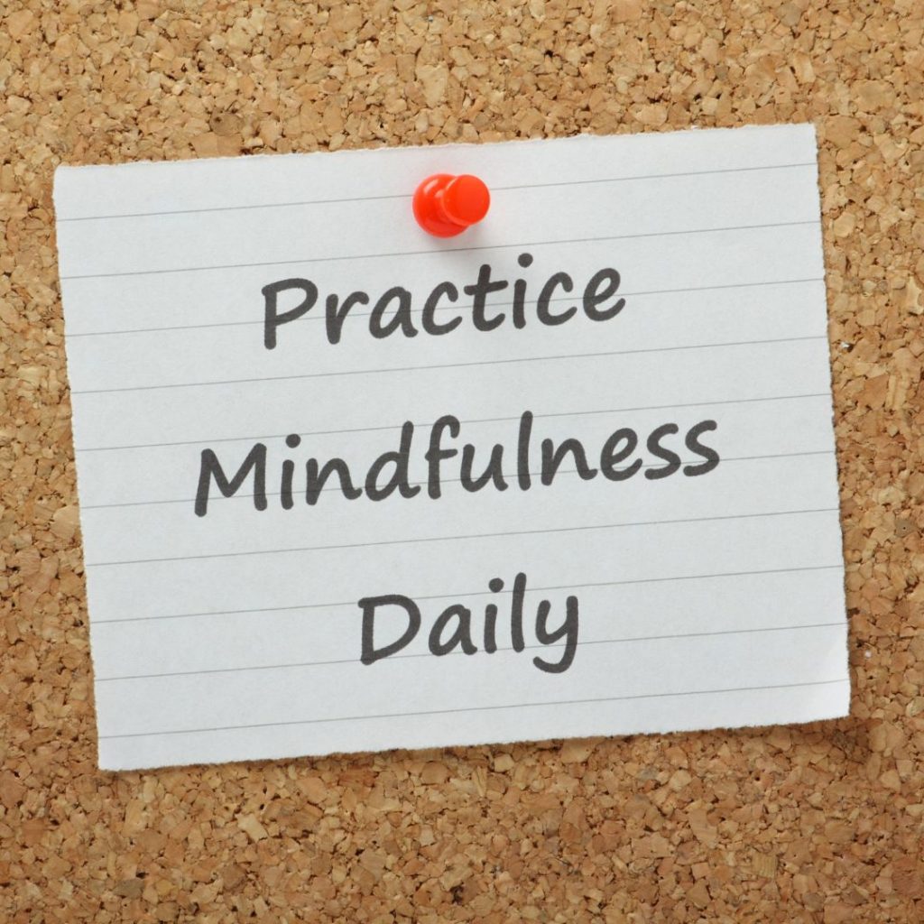 Practice Mindfulness Daily written in black on a square notebook paper and pinned to a board with red thumbtack.