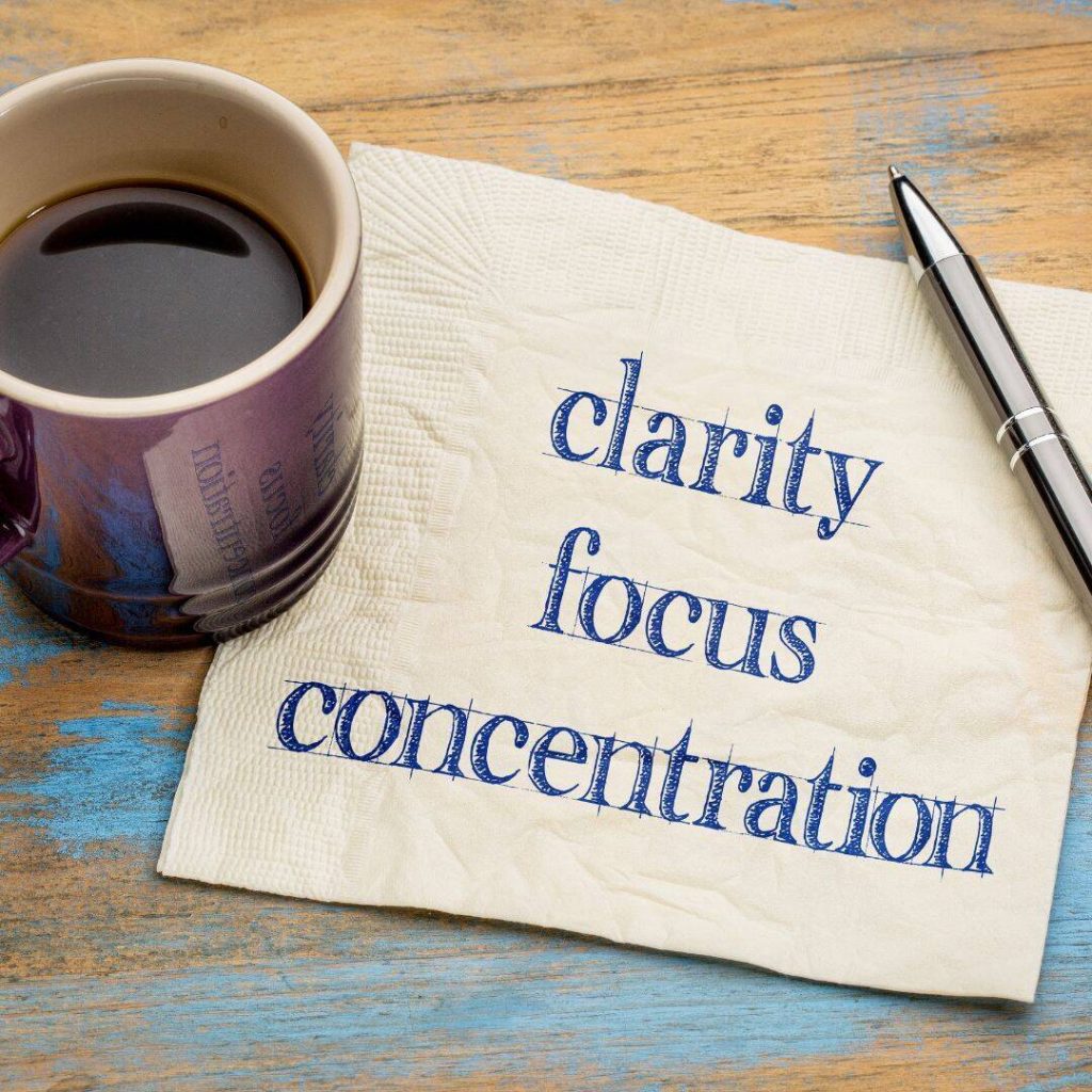 Coffee cup and pen next to a napkin with clarity, focus, and concentration written on it.
