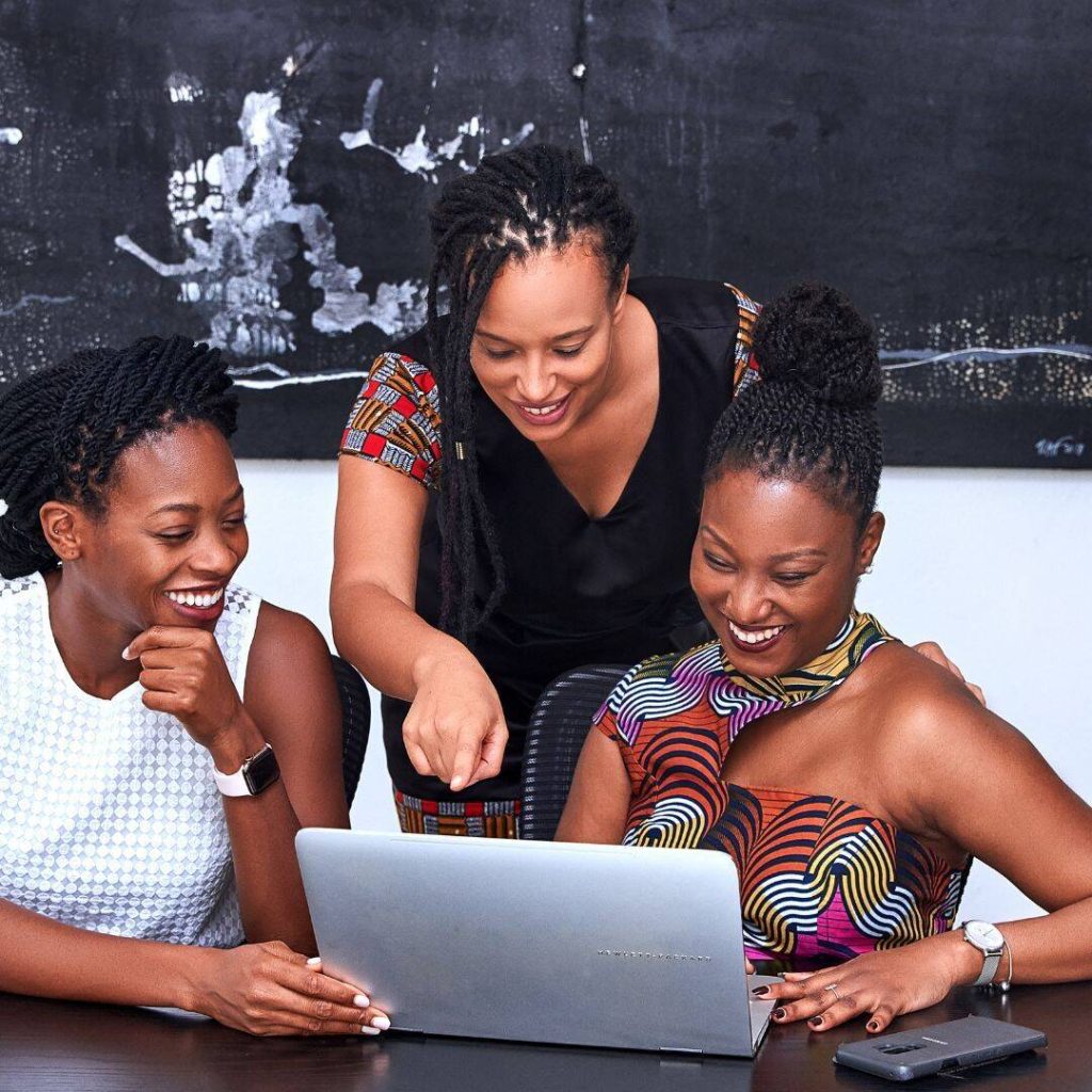 3 black women sitting in front of a laptop.  One woman is pointing at the screen.  They are collaborating and networking on ideas for a new book. 