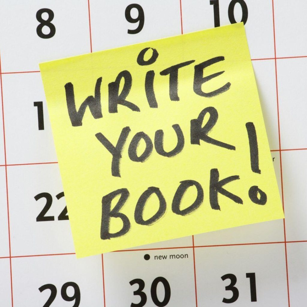 Bright yellow Post-it reads write your book in big black letters.  Post-it is placed on a calendar to demonstrate the writing schedule. 