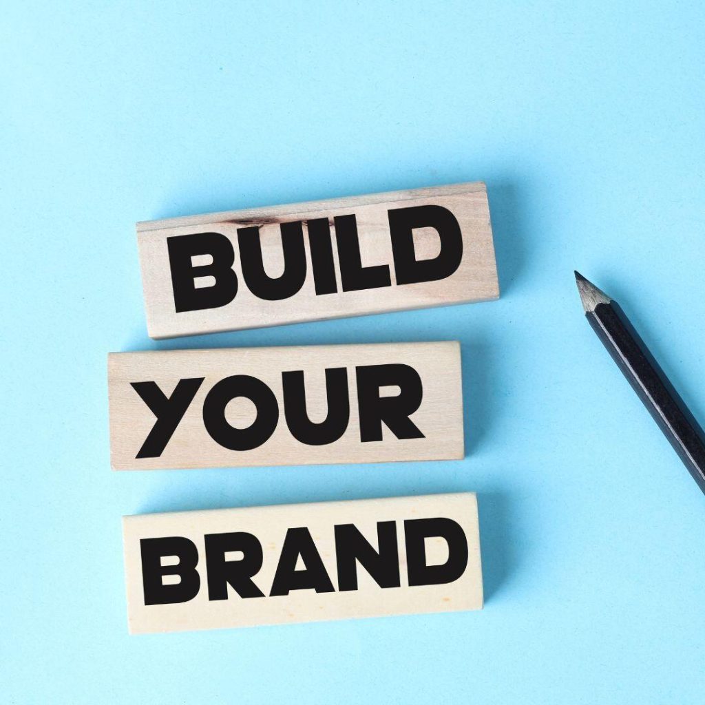 Build Your Brand written huge in black on three separate blocks for each word.  Light blue background and black pencil laying on the blue background.