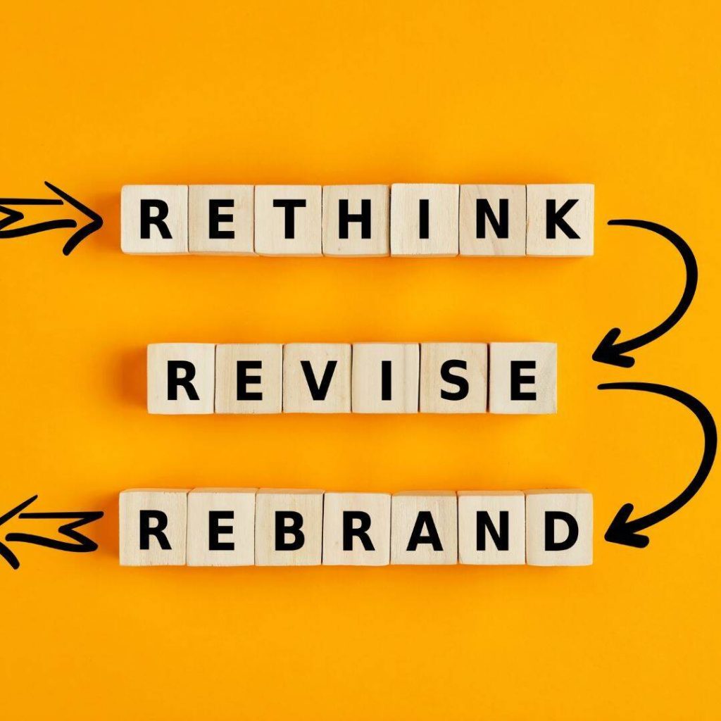 Rethink, Revise, and Rebrand.  Each letter for each word is placed on separate wooden blocks to spell out the words "Rethink, Revise, Rebrand."  Each letter is written in black.  The blocks are placed on a Golden yellow background.  Black arrows drawn from rethink, pointing down to revise.  A black arrow is drawn pointing down to the rebrand. 