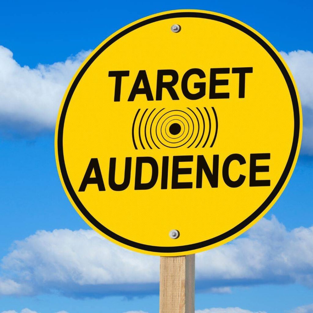 Target Audience written in huge black letters on a bright yellow sign.  The sign is shaped like a circle.  A cloudy blue sky is behind the sign. 
