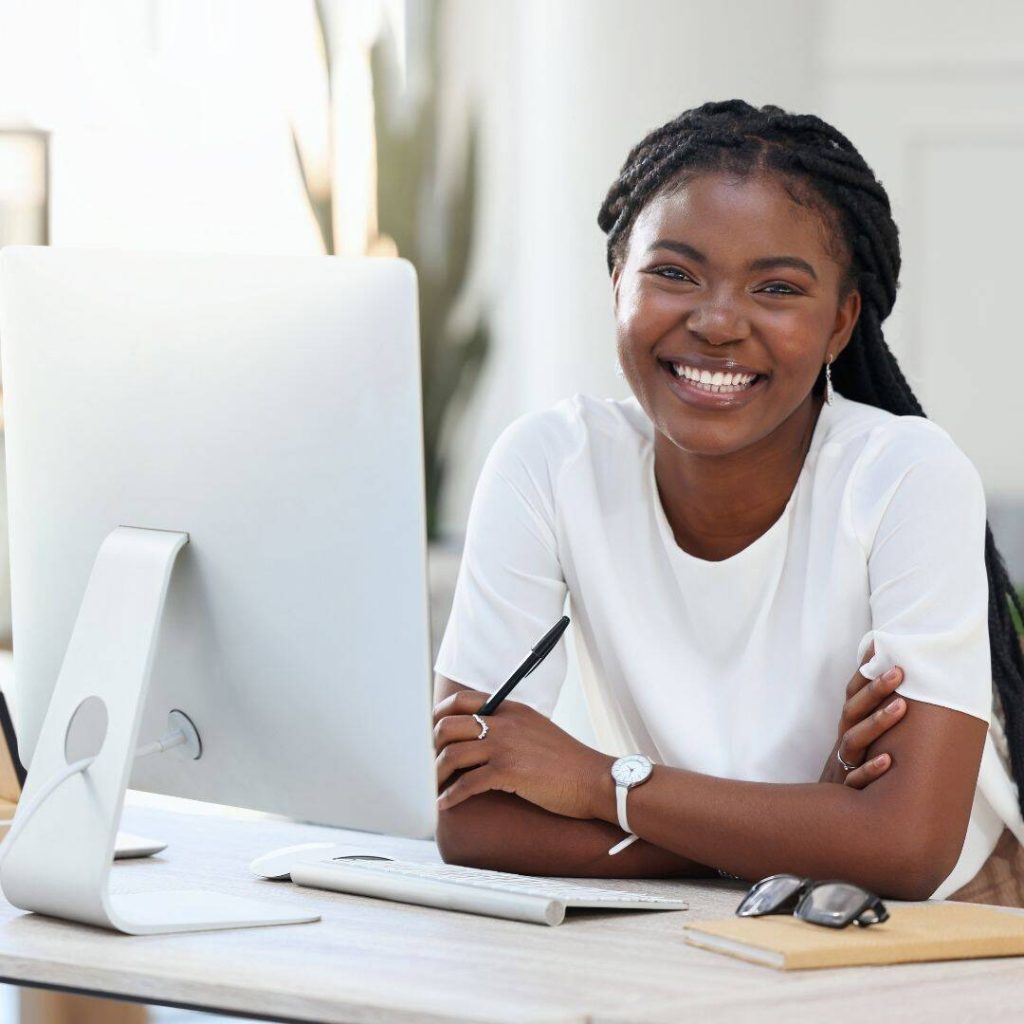 Black woman smiling in front of computer while doing market research.