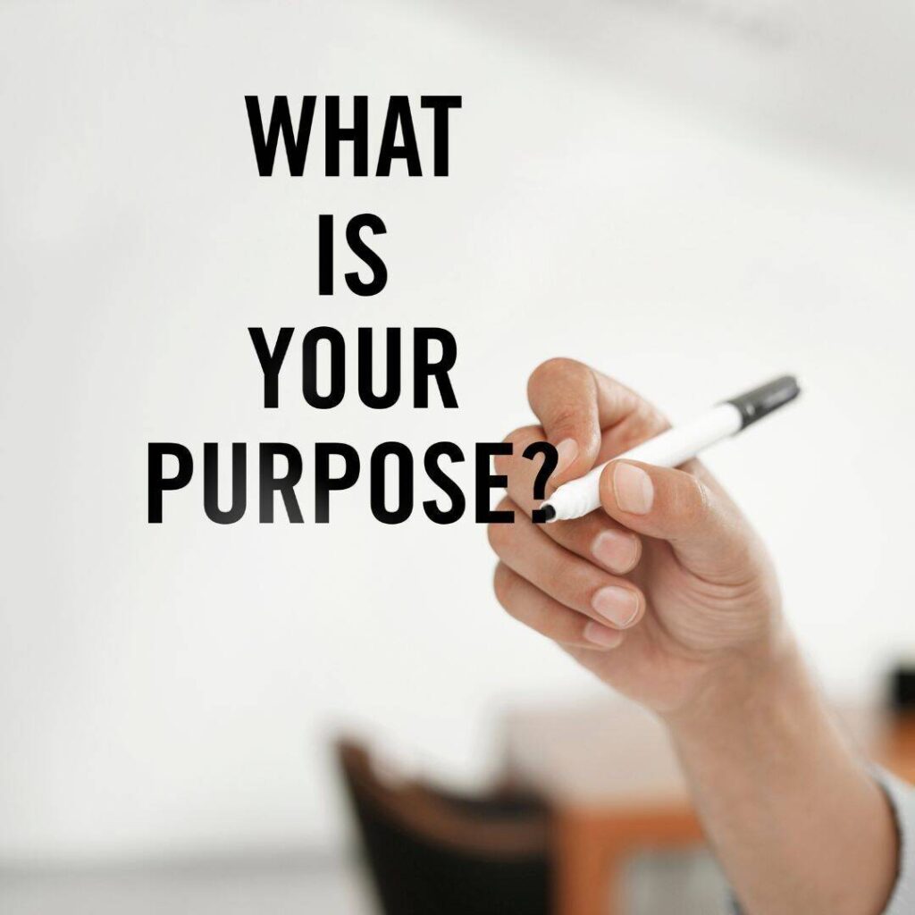 Black female hand writing what is your purpose written in black marker