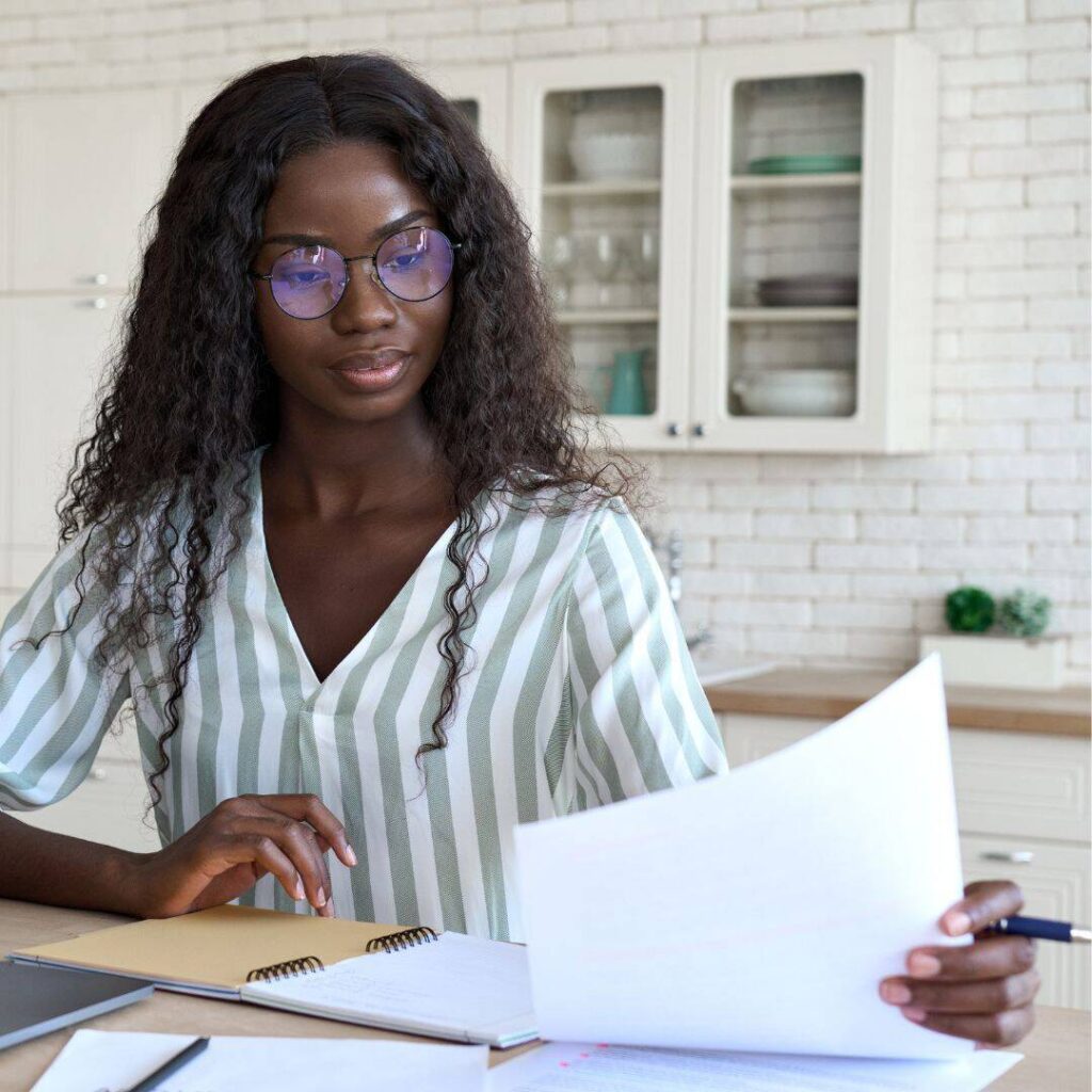 Woman wearing glasses reviewing her book manuscript and setting writing goals.  She's looking at 5 tips to start your book manuscript for aspiring writers. 