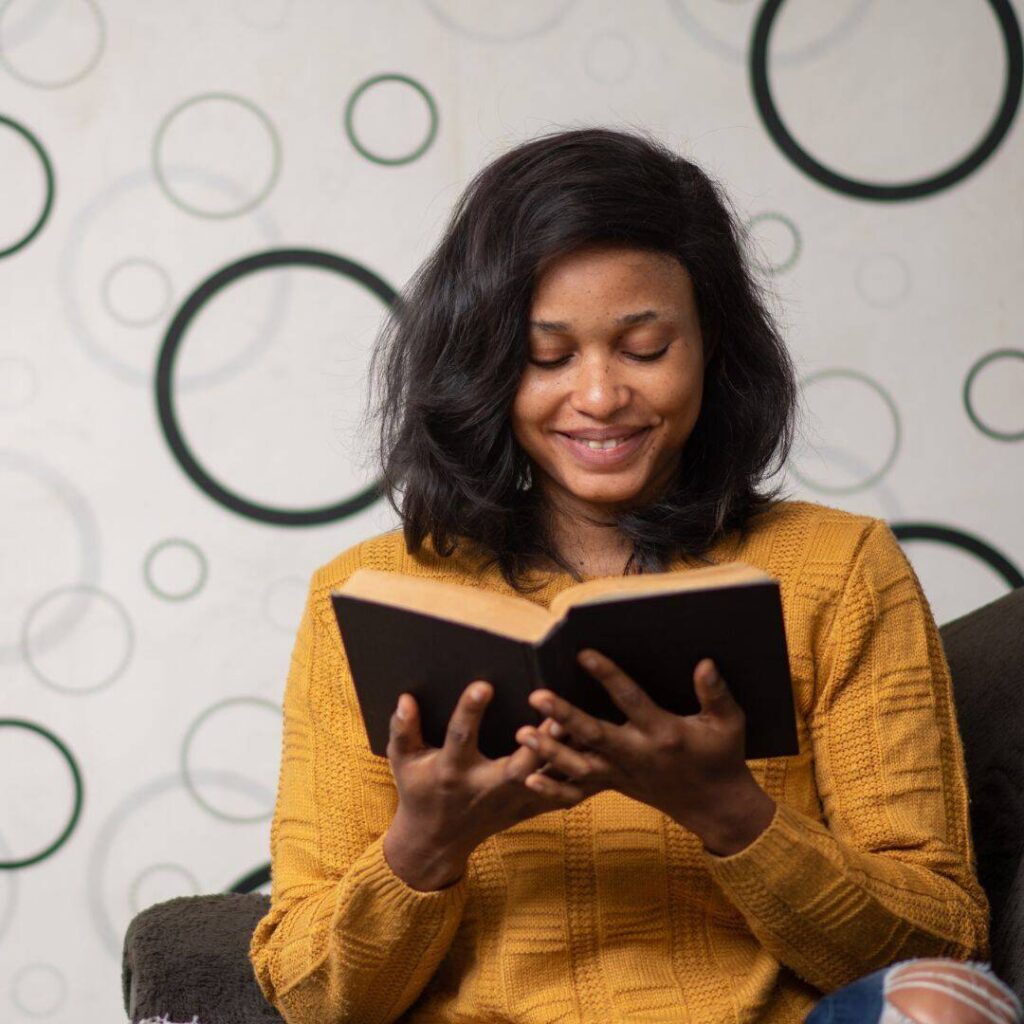 a black woman wearing a yellow blouse  smiling while reading a book as empty circular shapes surround her.